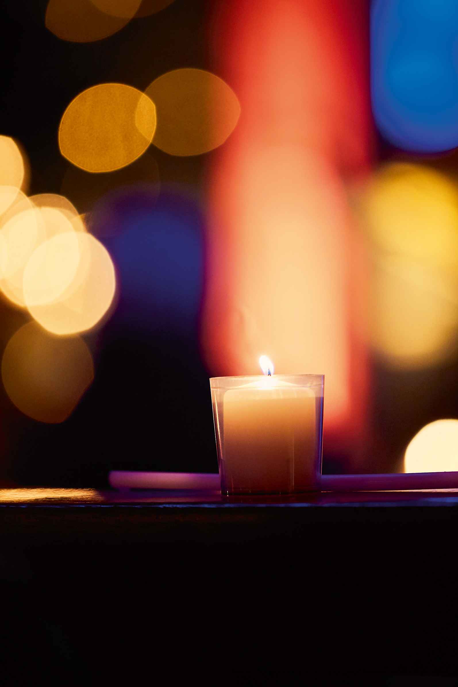 Eine Kerze im Pilgerkloster Werl. Im Hintergrund leuchten verschiedene Farben verschwommen.