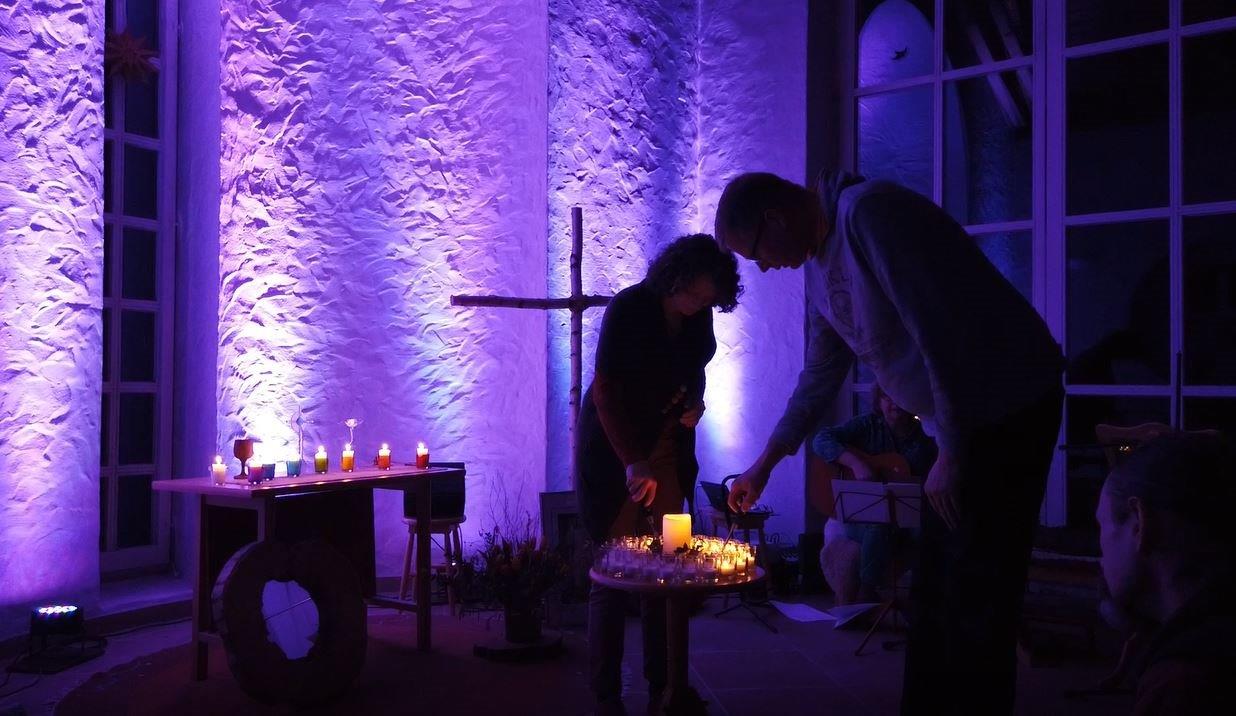 Ein Mann und eine Frau zünden Kerzen in der violett beleuchteten Kapelle der Lebensgemeinschaft St. Raphael an.