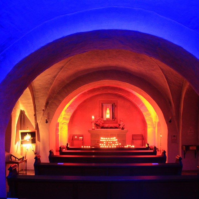 Rot und gelb erleuchtete Krypta im Kloster Oelinghausen während einer Veranstaltung zu "finde dein Licht". Mittig im Bild sieht man eine Madonnen-Statue. © Veronika Schulte.