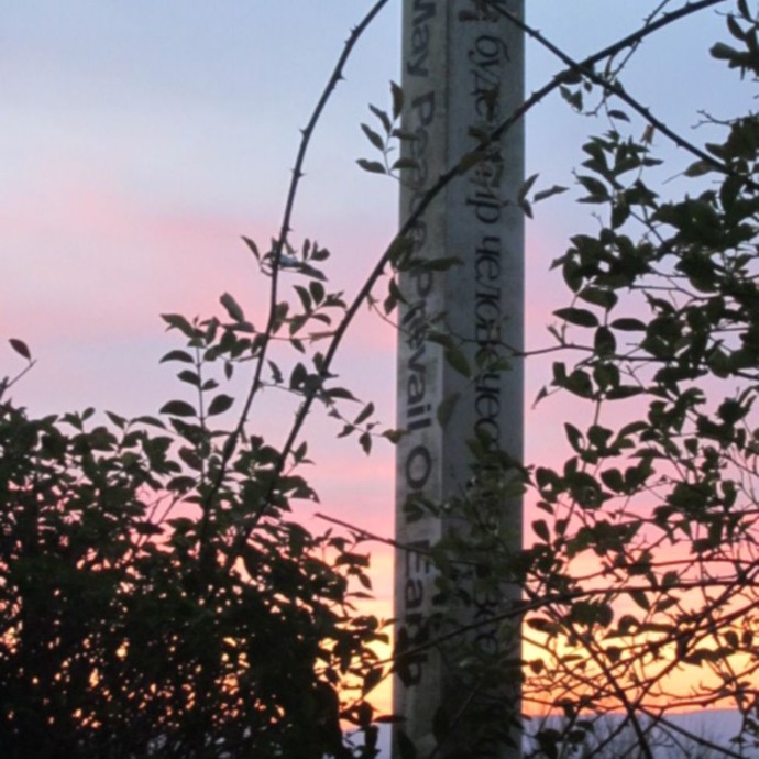 Friedenspfahl bei Sonnenuntergang mit Inschrift „May Peace Prevail On Earth“ („Möge Frieden sich auf Erden durchsetzen“). © Manuela Baumann.