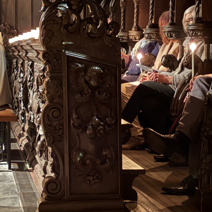 Besucher:innnen sitzen mit Kerzen in der Hand in Bankreihen der Kirche. (vergrößerte Bildansicht wird geöffnet)